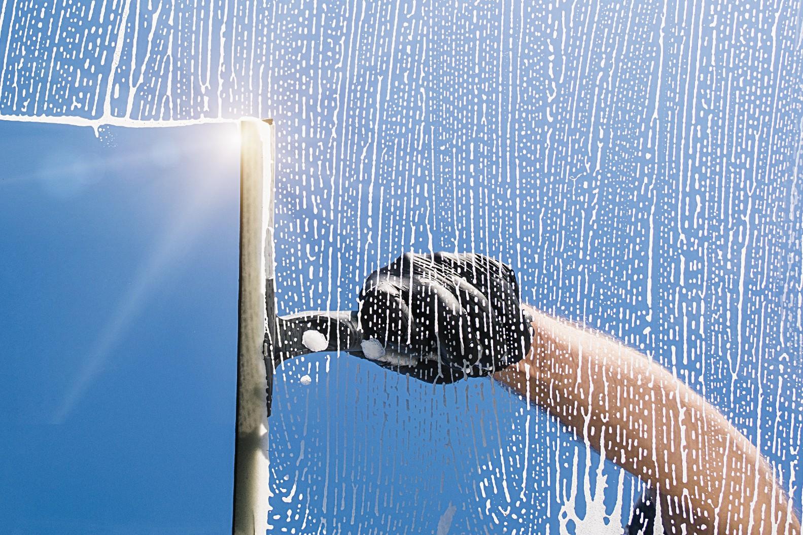 A person cleaning a window in bright sunlight, which you should not do because it leaves streaks.