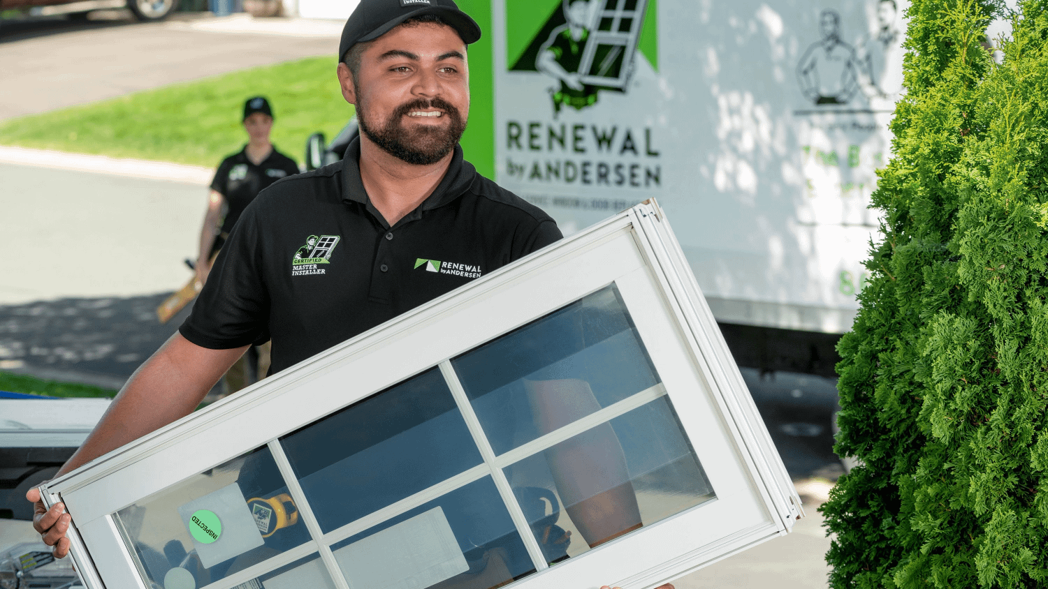 A Renewal by andersen installer carrying a white window towards a home for replacement