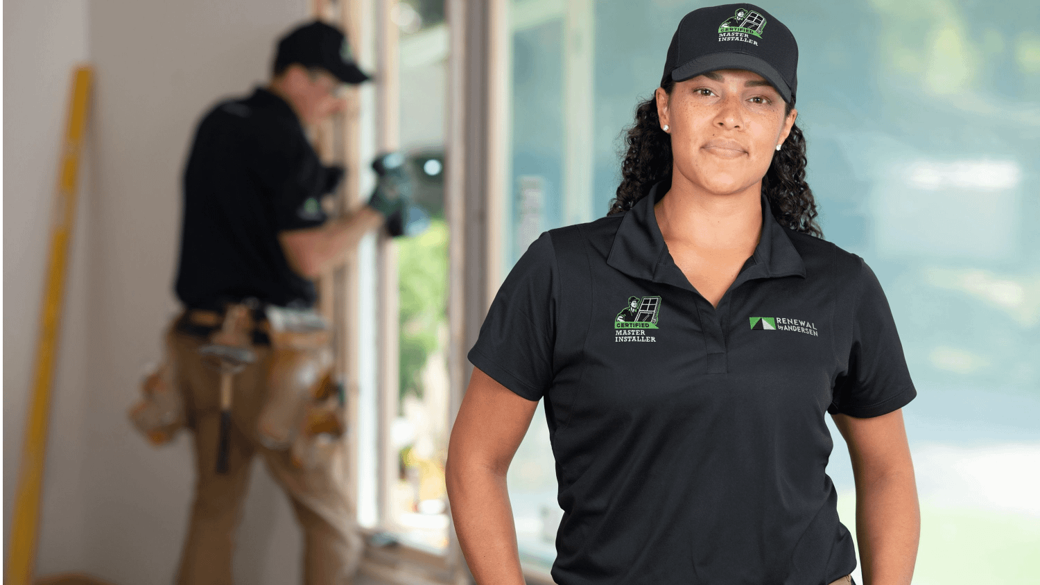 Renewal by andersen female installer standing infront of a window, while there is another installer in the background tightening the windows