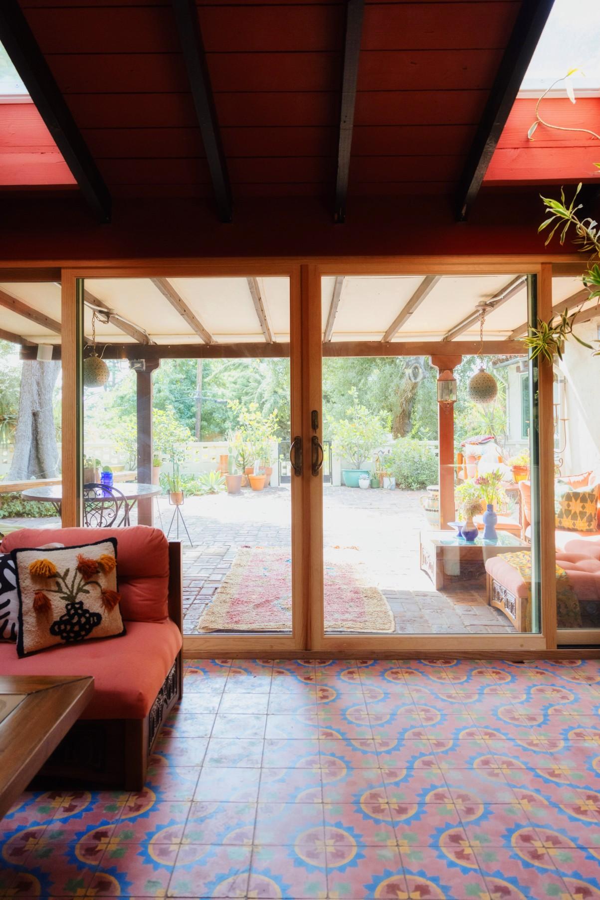 A modern glass sliding door with a wood interior. The room has a brightly colored tiled floor and a couch/