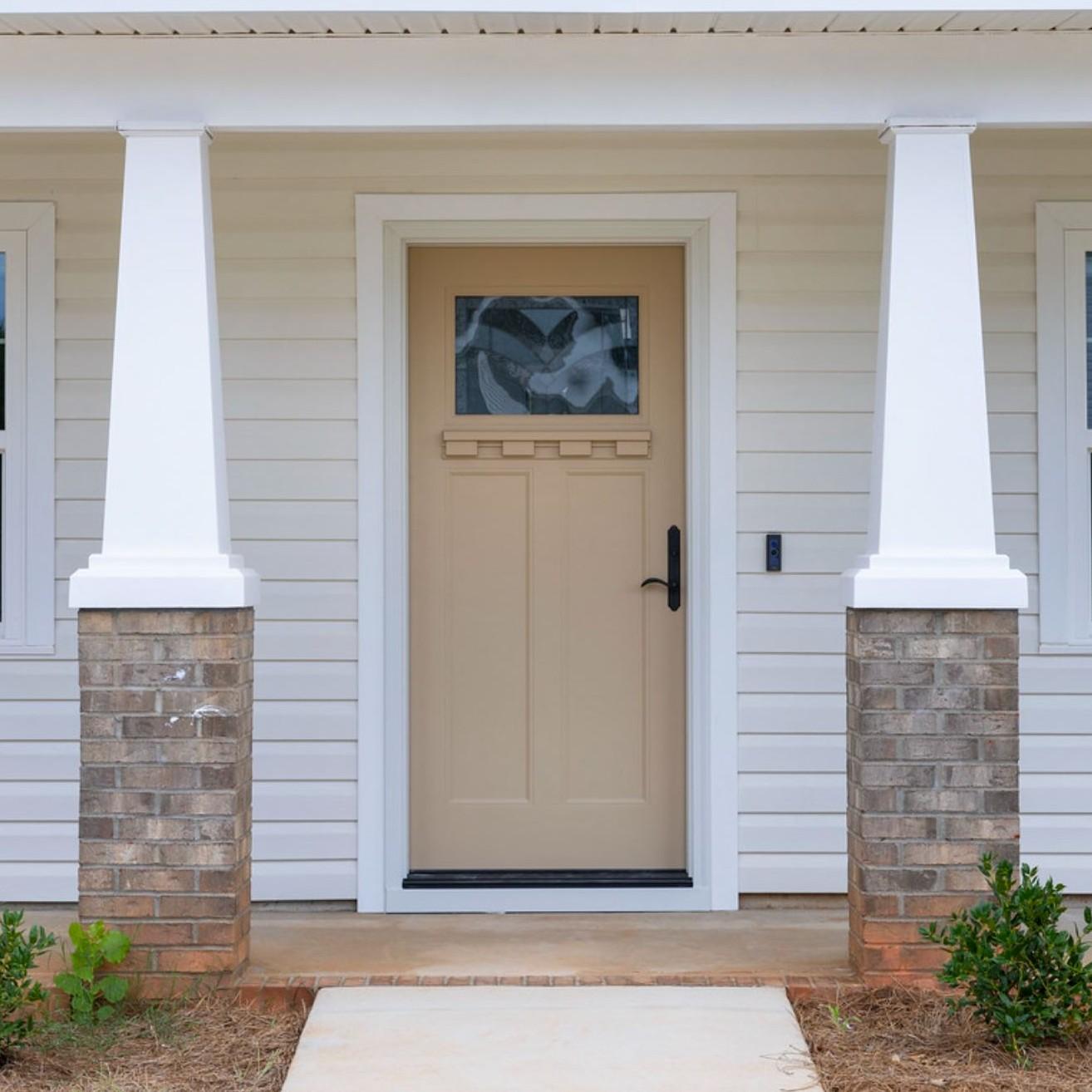 A single panel Ensemble entry door. The door is tan and has a small art glass panel and a dentil shelf. It is flanked by columns.