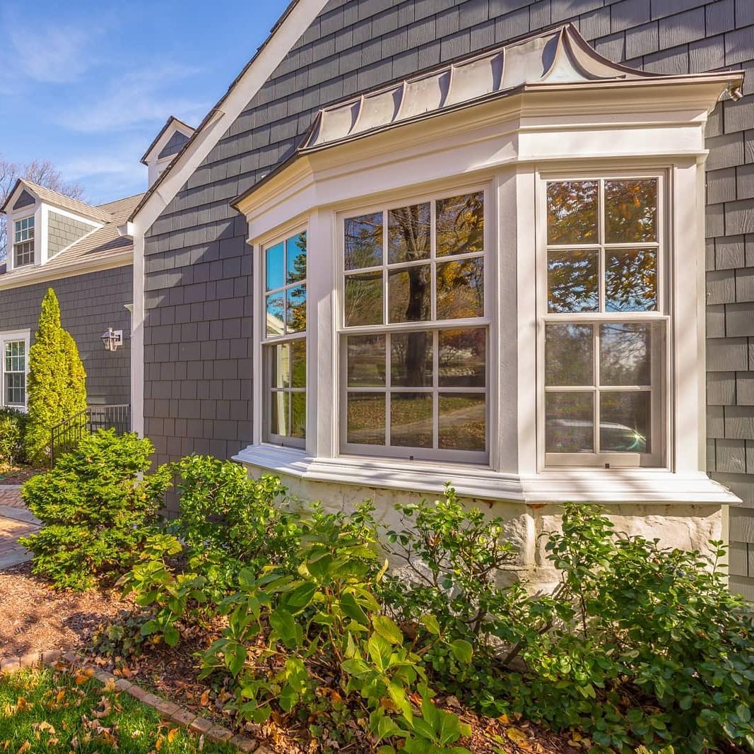 A cape cod style home with grey siding and a bay window.