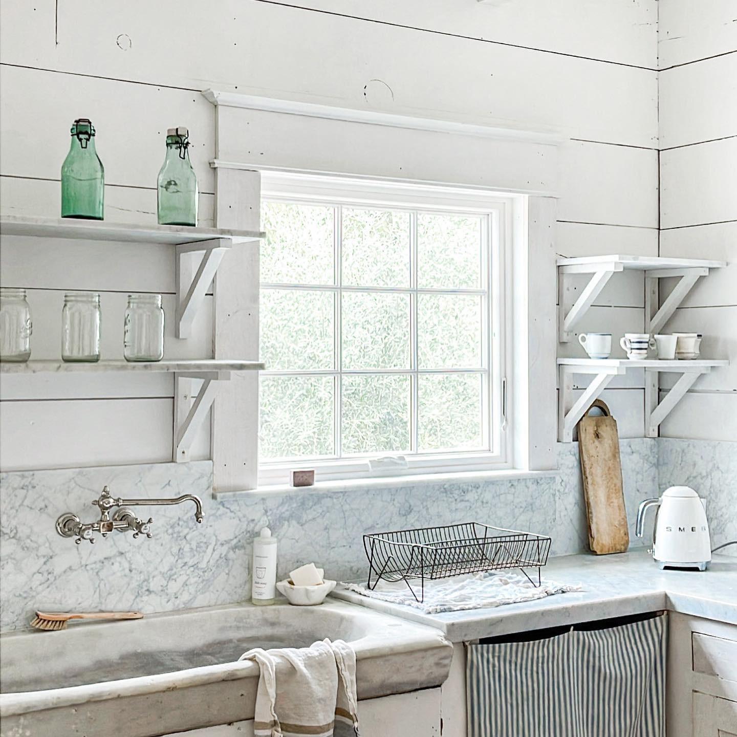 A white farmhouse kitchen with a casement window behind the sink. The window has colonial grilles.