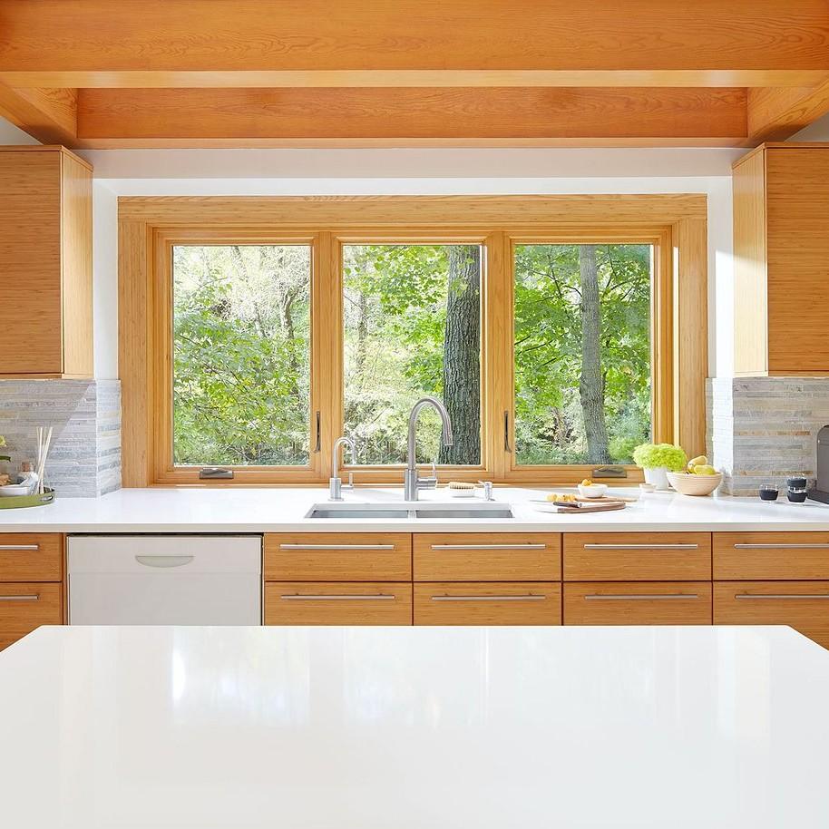Wood interior casement windows in a bank behind a kitchen sink and a long, white granite counter.