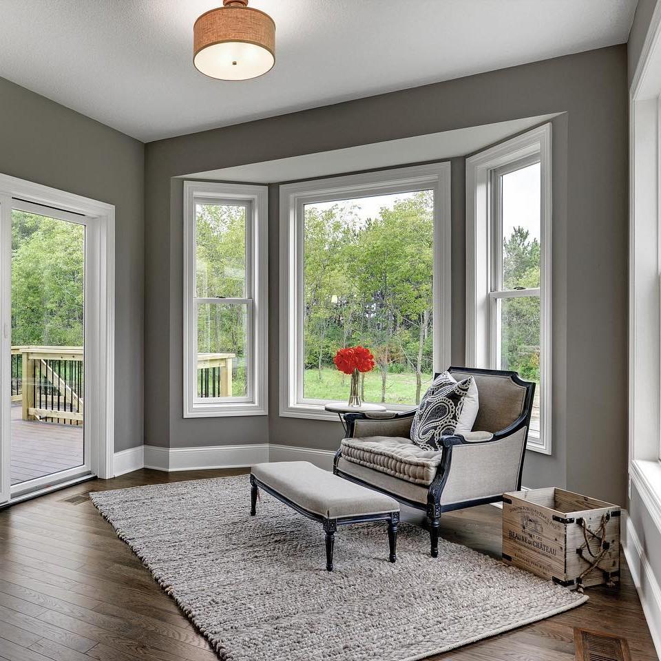 A dining room or reading nook with grey walls and a bumped out section that has a picture window facing the back yard.