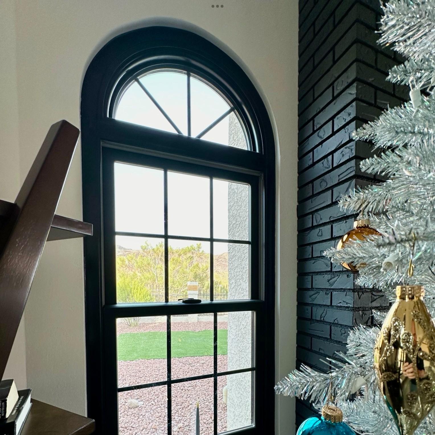 A black double-hung window topped with a circle top window. There is a Silver flocked Christmas tree near by.