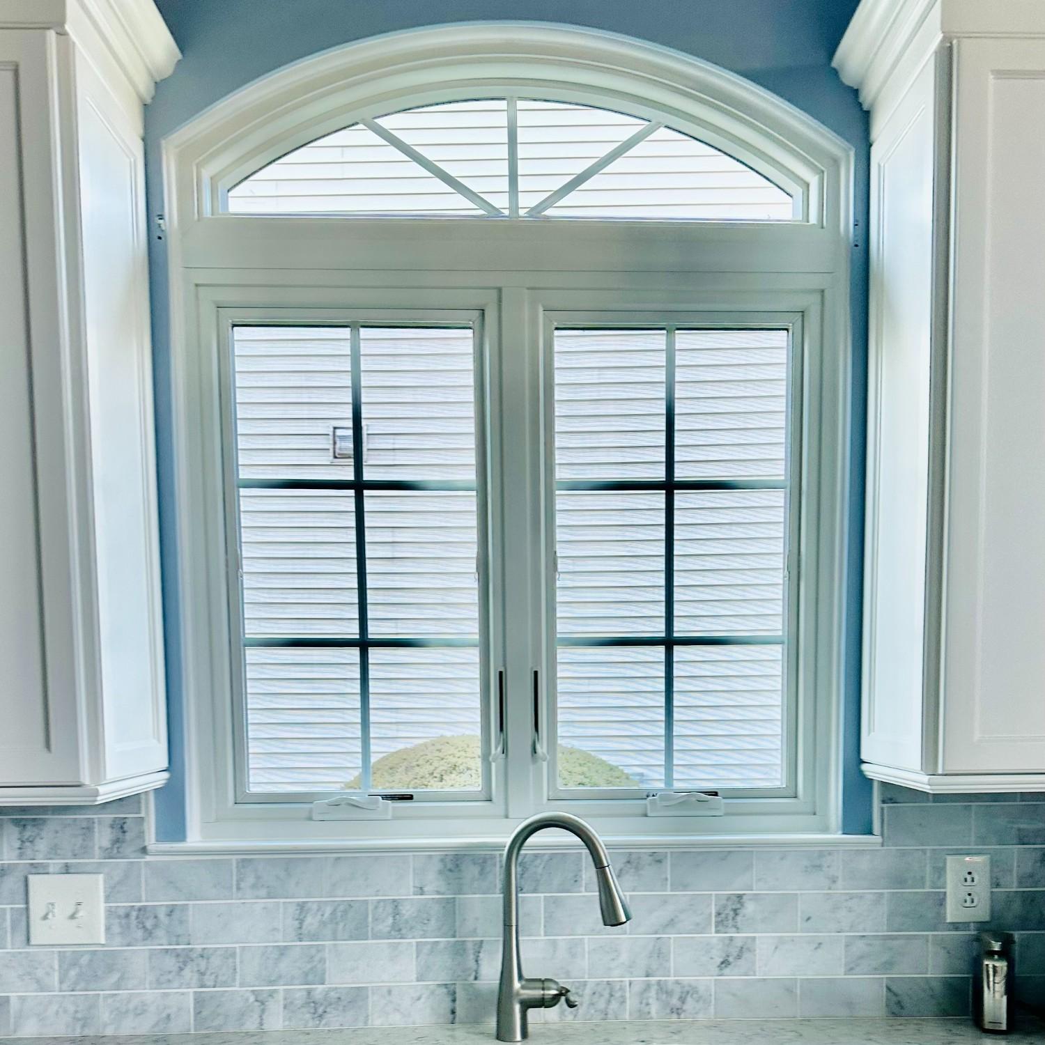 An equal leg arch with sunburst grilles above two casements. The window is white and in a kitchen above sink and between white cabinets.